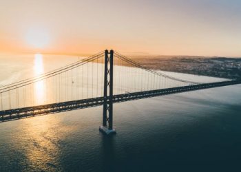 image00015 Aerial view suspension bridge over Tagus river in Lisbon. Drone flying above water opposite 25th april bridge symbol of Portugal in sun shining, beautiful landscape at sunset.