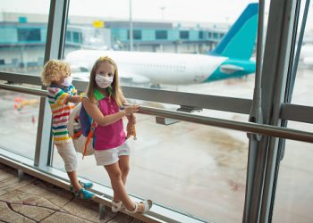 image00001bis Kids at airport in face mask. Children look at airplane after coronavirus outbreak. Safe travel and flying with child in virus pandemic. Family at departure gate. Vacation after covid-19 lockdown.